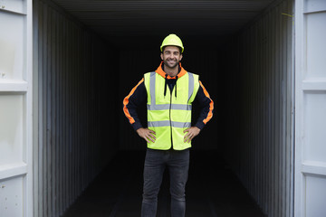 Smiling guy in hard hat standing by container, portrait