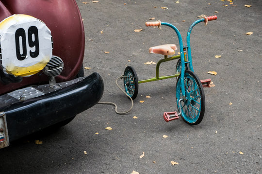 Retro three wheel children bicycle near a retro car in the street