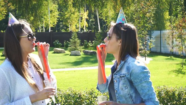 two young woman in party hat blowing in party horn