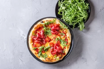 Crédence de cuisine en verre imprimé Pizzeria Whole homemade pizza with cheese and bresaola, served on black plate with fresh arugula over gray concrete texture background. Flat lay.