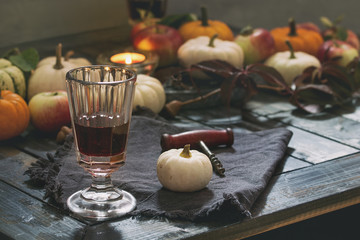 Autumn holiday table decoration setting with decorative pumpkins, apples, red leaves, glasses of red wine, candle over wooden table. Rustic style, day light