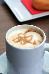 Cup of foamy cappuccino on a plate on a wooden table.