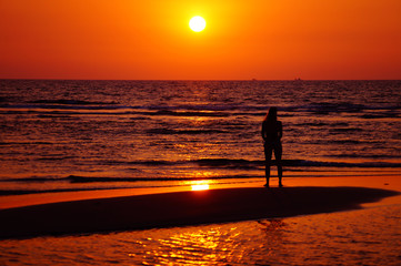 Woman stand on the beach and look to the sunset. Female in bikini on the beach. Woman silhouette. Fitness model with sport body.