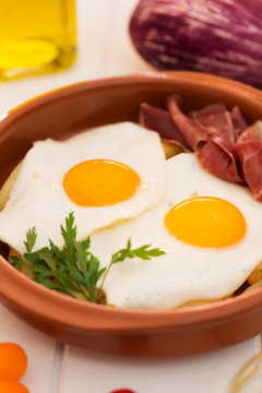 Fried eggs in a ceramic cup with spanish jamon for breakfast on a white background. Close up