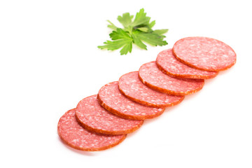 Smoked salami sausage. Sliced smoked sausage salami isolated on white background. Pieces of smoked sausage decorated with parsley leaves. Neatly sliced smoked sausage for advertising. Space for text.