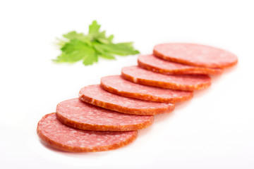 Smoked salami sausage. Sliced smoked sausage salami isolated on white background. Pieces of smoked sausage decorated with parsley leaves. Neatly sliced smoked sausage for advertising. Space for text.