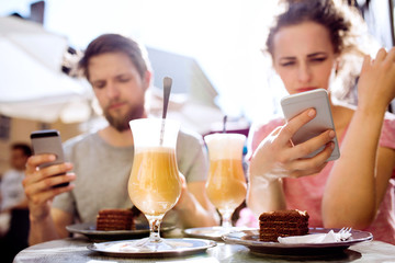 Young couple with smartphones sitting in cafe.