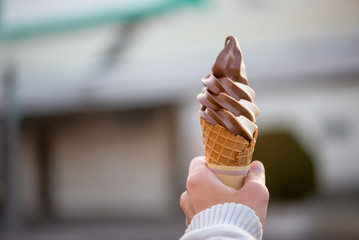 Close-up detail of a chocolate vanilla twist soft serve in a crispy, homemade waffle cone, with blurred background and sweater hands. Nobeoka, Japan. Travel and food concept. - 175211158