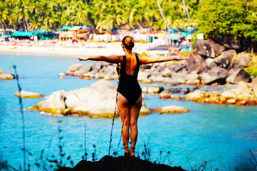 Young and pretty girl in a swimwear are ready to jump from the rock. Palolem beach, Goa, India. Sexy female body. Colorful beach on the background.