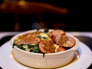 The selective focused and closeup image of braked spinach with cheese and sausage in a whit bowl.