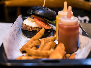 The selective focused and closeup image of black burger served with fried potato in a tray