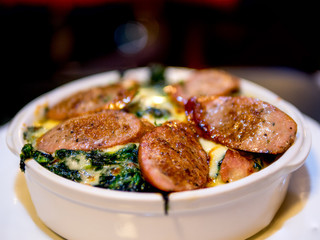 The selective focused and closeup image of braked spinach with cheese and sausage in a whit bowl.