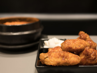 The selective focused and closeup image of Korean style fried chicken in black plate with pickle Chinese radish and a bowl of Kimchi soup in black background
