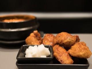 The selective focused and closeup image of Korean style fried chicken in black plate with pickle Chinese radish and a bowl of Kimchi soup in black background