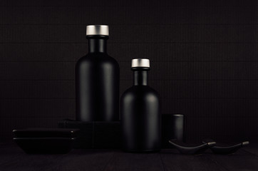 Obraz na płótnie Canvas Dark black minimalist interior. Blank black cosmetics bottles on dark wood board with copy space. Noir elegant home decor for advertising, designers, branding identity, cover.