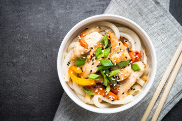 Udon stir-fry noodles with chicken and vegetables on black stone table. Top view copy space.