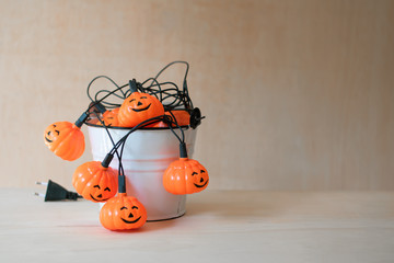 Halloween garland inside a white bucket on a wooden table. Jack-O-Lantern. Electric lights.
