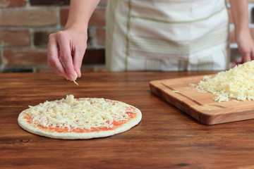 Woman make pizza, sprinkles cheese on the dough
