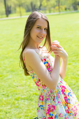 Portrait of young beautiful woman with long hair wearing flower dress in green spring park