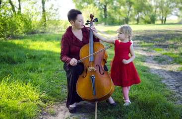 Grandmother and granddaughter playing outdoors on cello. Adult woman teaching girl to play violoncello