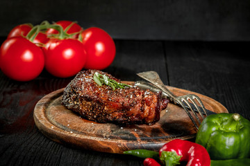 Grilled steak seasoned with spices and fresh herbs served on a wooden board with fresh tomato and red and green peppers
