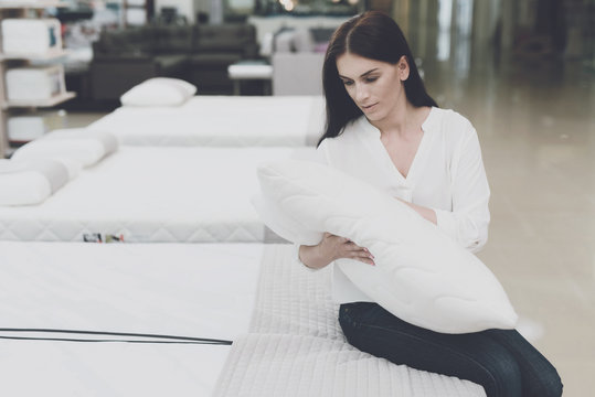 A woman picks herself a pillow in a large store. She sits on the bed and examines her. She is holding it in her hands