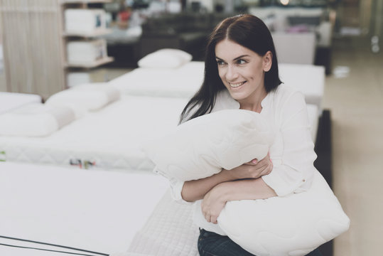 A woman picks herself a pillow in a large store. She sits on the bed and examines her. She sits and hugs her