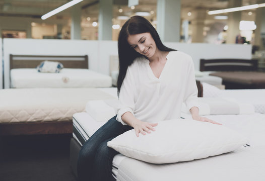 A woman picks herself a pillow in a large store. She sits on the bed and examines her. She sits and examines her