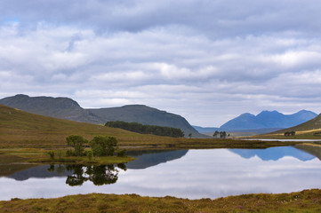 Beautiful lake with reflections of the trees and surrounding mountains in the Scottish Highlands, in Scotland, United Kingdom; Concept for travel in Scotland