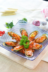 Mussels with tomato in purple glass plate on wooden cutting board