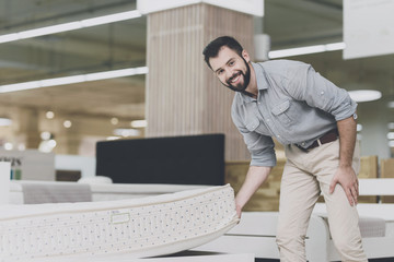 A man inspects a mattress in a mattress store. He lifted one of them