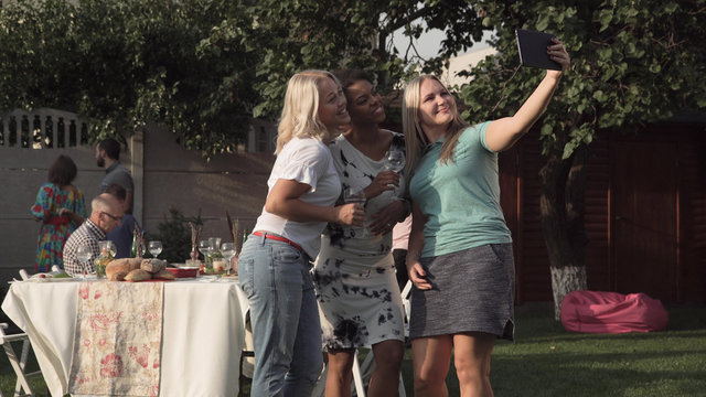 Multiracial group of women communicating and taking selfie shot with digital tablet on family party.