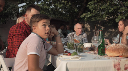 Bored young boy feeling annoyed sitting at table on family reunion party.