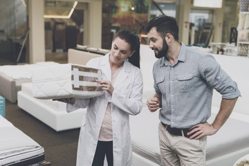 An orthopedic woman shows the man a sample of the mattress he wants to buy