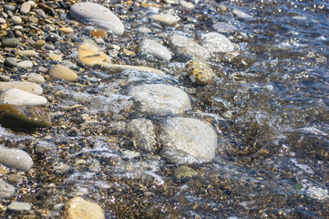 sea pebble beach with multicoloured stones, waves with foam