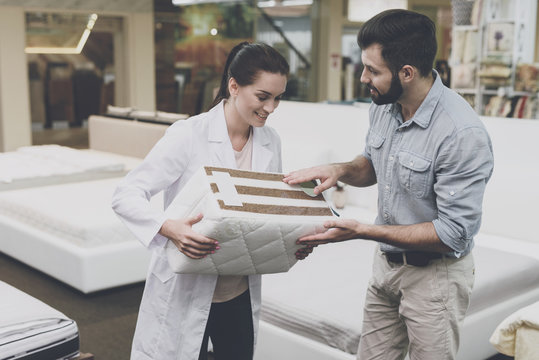 An orthopedic woman shows the man a sample of the mattress he wants to buy