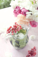 Cooling mint detox water with a branch of viburnum and a bouquet of pink and white peonies on pastel pink background.