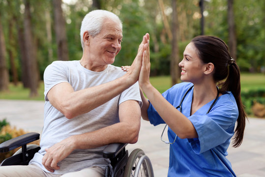 A nurse and an old man in a wheelchair high five in a summer park