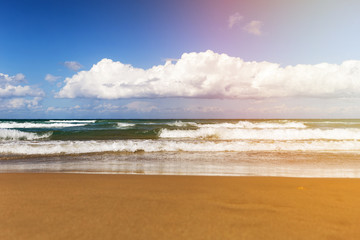 Sunny day on the beach with big waves and white clouds