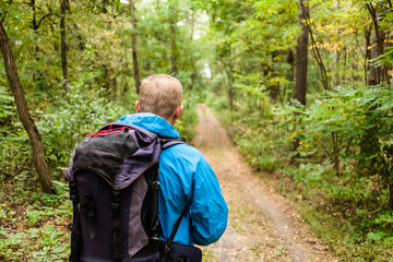 Hiker with backpack is walking in the autumn forest.