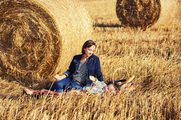 Naklejka na ściany i meble Happy mother and 2 year old girl next to hay bales in harvested field