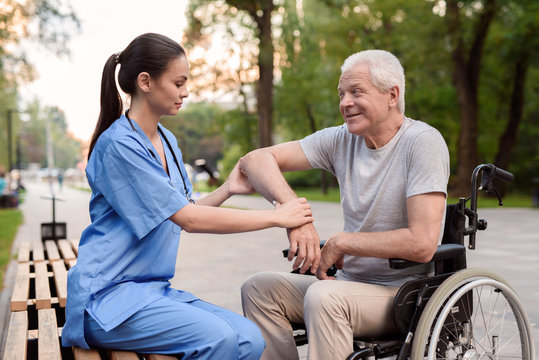 A nurse carefully examines the elbow of an elderly patient on a bench in the park