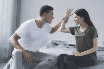 A man sits on the bed and holds the hand of a woman who sits next to him and wants to hit him
