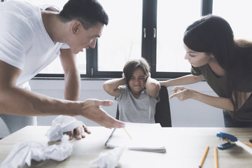 A man and a woman are standing over a table, behind which sits a girl who covered her ears with her hands