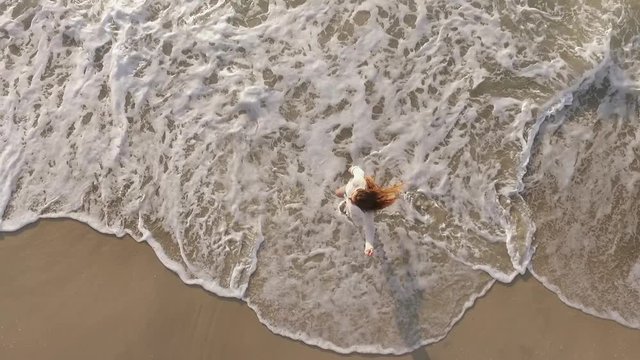 rapid footage view from above joyful enegetic woman barefoot running along seaside playing with waves enjoying life at sunset 
