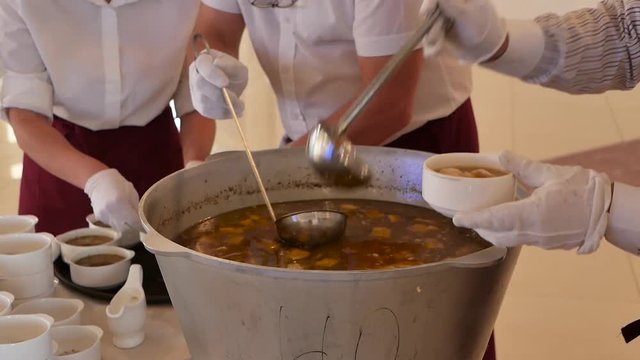 waiters from a metal boiler pour soup of dishes