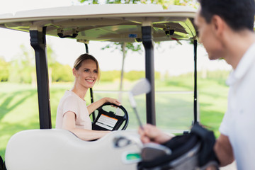 A man pulls out a golf club from the bag, a woman sits behind the wheel of a golf car