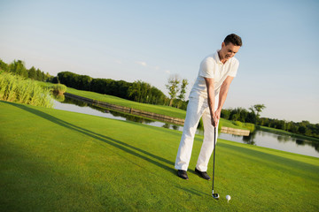 A man is standing on a golf course and getting ready to hit the ball with a golf club