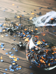 Halloween orange and black confetti with spiders and spider net on dark rustic wooden background. Holiday decoration symbols