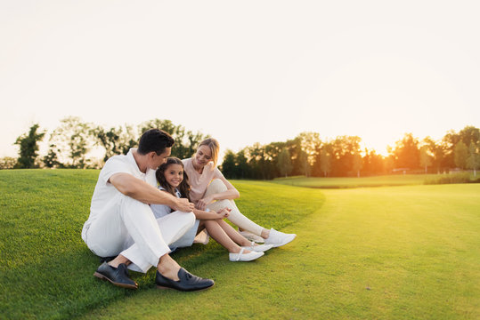 Happy family resting on a golf course sitting on the grass on a sunset background